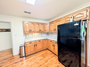 A kitchen with wooden cabinets, a black refrigerator, and a stainless steel trash can. - The Hilltop Farmhouse (Mena)