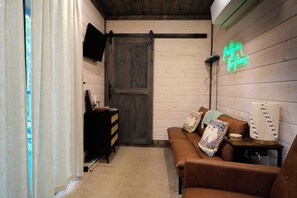 A cozy room with a brown leather sofa, a wooden door, a black TV on the wall, and a neon sign. - Pretty in the Pines- *Near WPG* (MENA)
