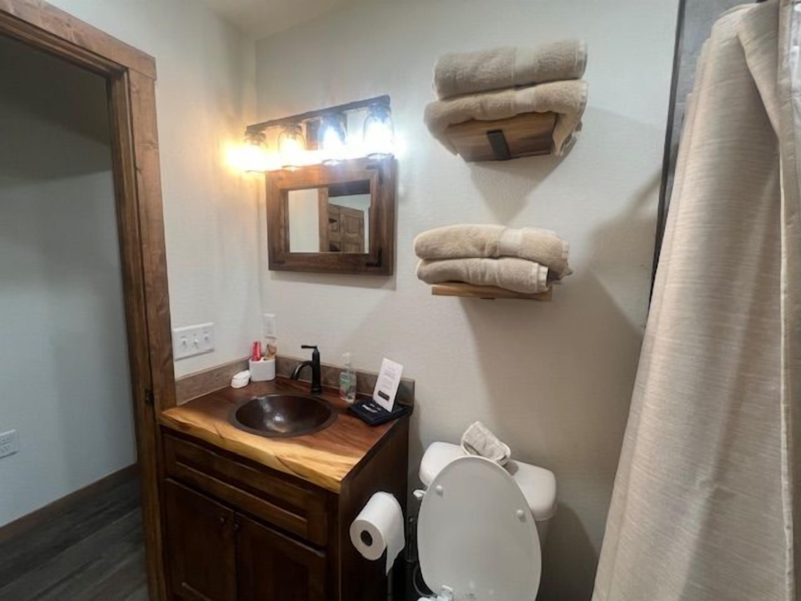 A bathroom with a wooden vanity, a sink, a toilet, and towels on shelves.