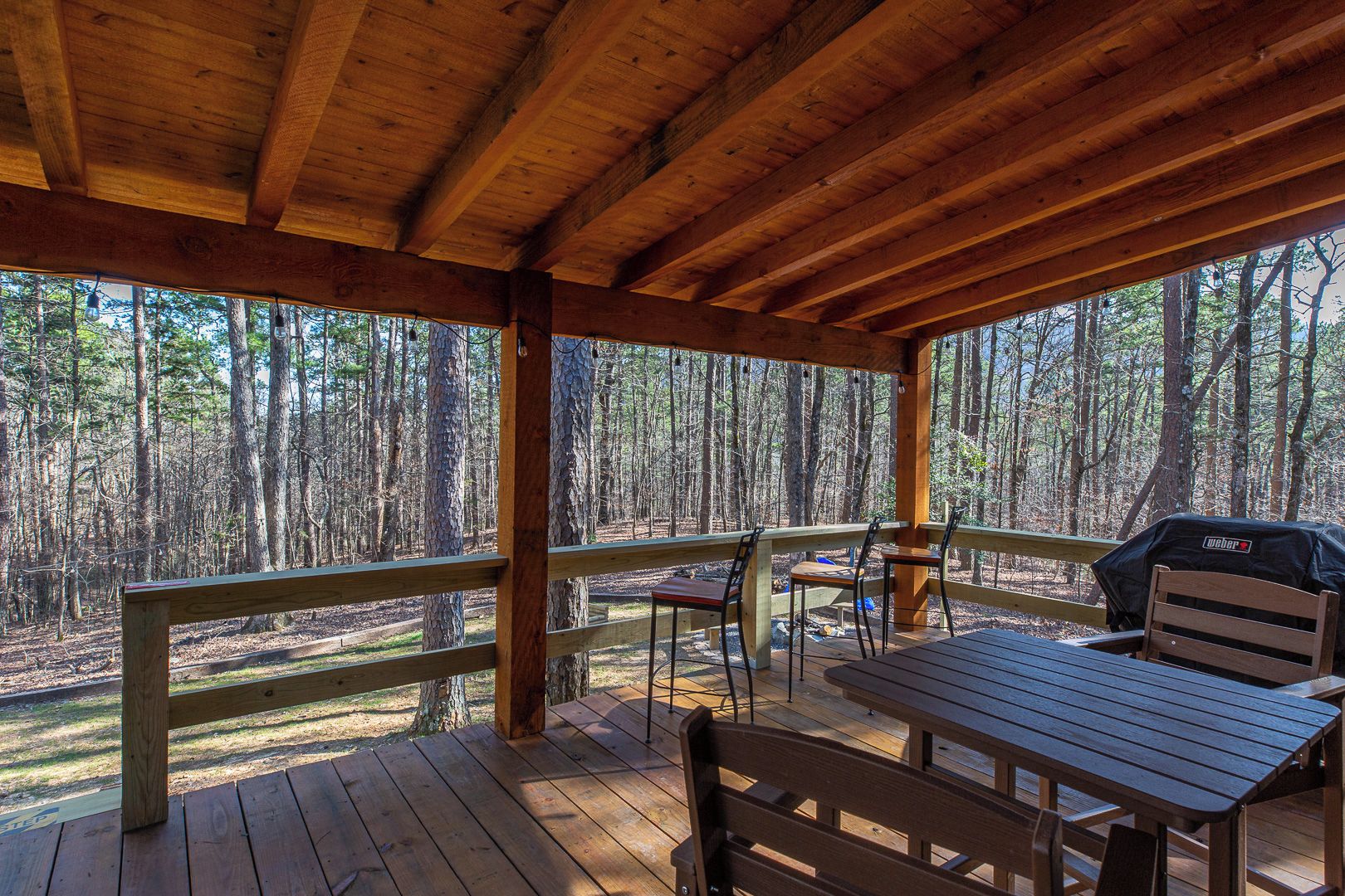 Eine überdachte Holzterrasse mit Picknicktischen und -stühlen mit Blick auf ein bewaldetes Gebiet.