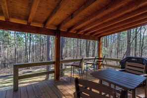 A covered wooden deck with picnic tables and chairs, overlooking a forested area. - Whispering Pines - Side by Side Cabins in Shady! (Mena)