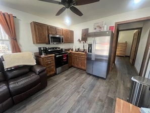 A compact kitchen with wooden cabinets, a microwave, a stove, and a refrigerator. - Whispering Pines Guest Cabin near Wolf Pen Trails! (Mena)