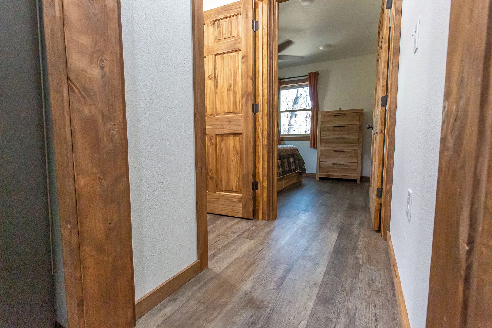 A hallway with wooden doors, a bed with a window, and a dresser.