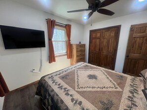 Un dormitorio con cama, televisor montado en la pared, ventilador de techo y puertas de madera.