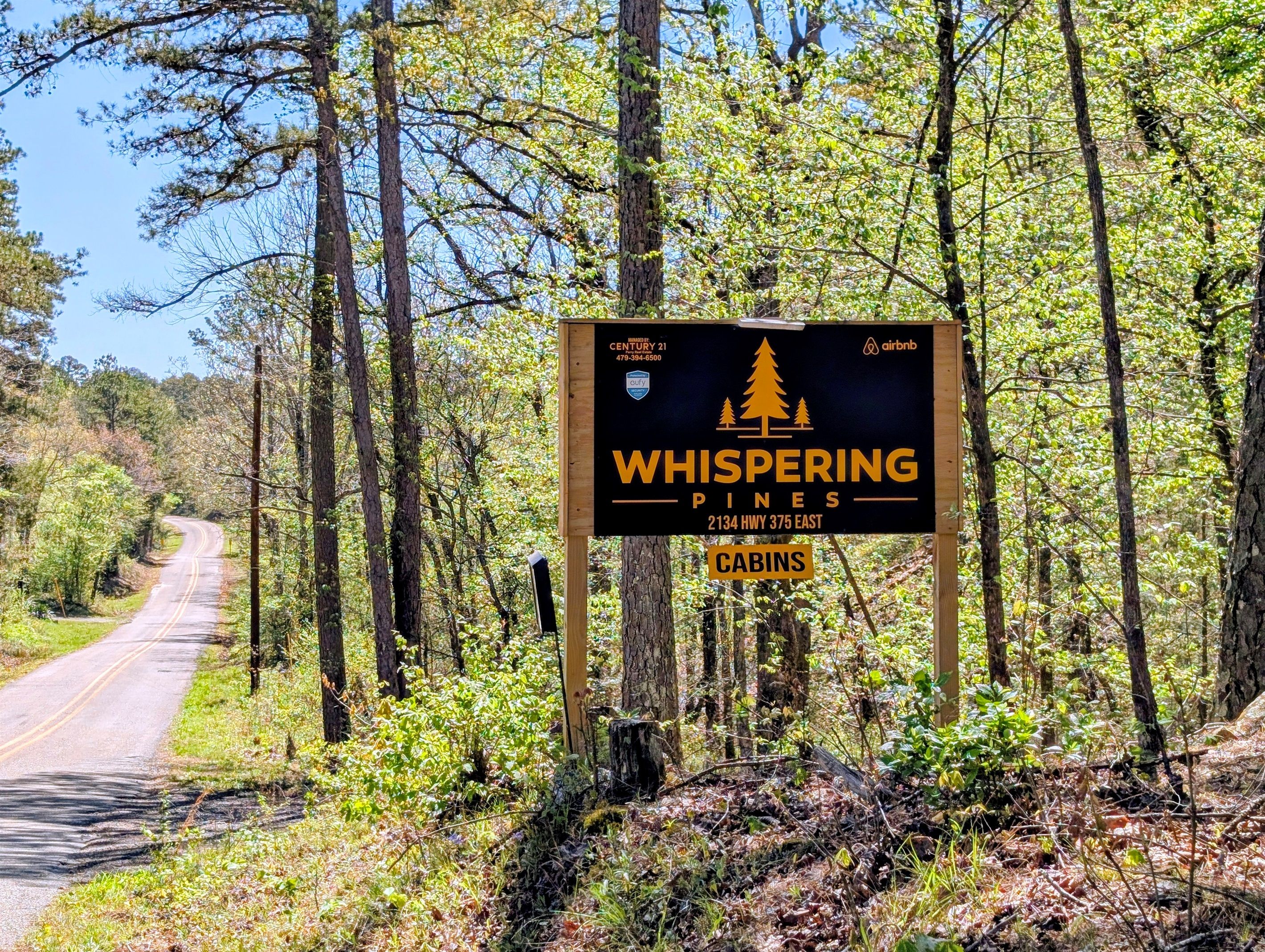 A sign for Whispering Pines cabins with a two-lane road in the background.