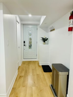 A hallway with a white door, a small plant, a fire extinguisher, and a black mat. - Private Bsmt Apt W/Separate Entry- 1 Min to Subway (Oak Park)