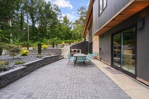 A modern outdoor patio with a brick floor, a wooden deck, and a dining area with chairs and a table. - The SB Gallery House Unapologetically Different (Raleigh)