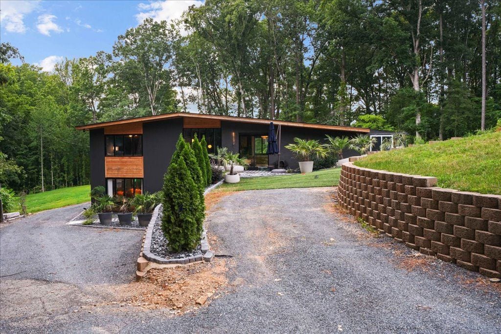 A modern house with a gravel driveway, surrounded by a landscaped garden and tall trees.