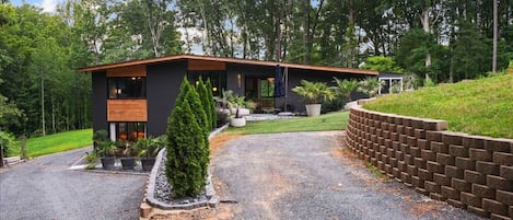 A modern house with a gravel driveway, surrounded by a landscaped garden and tall trees.