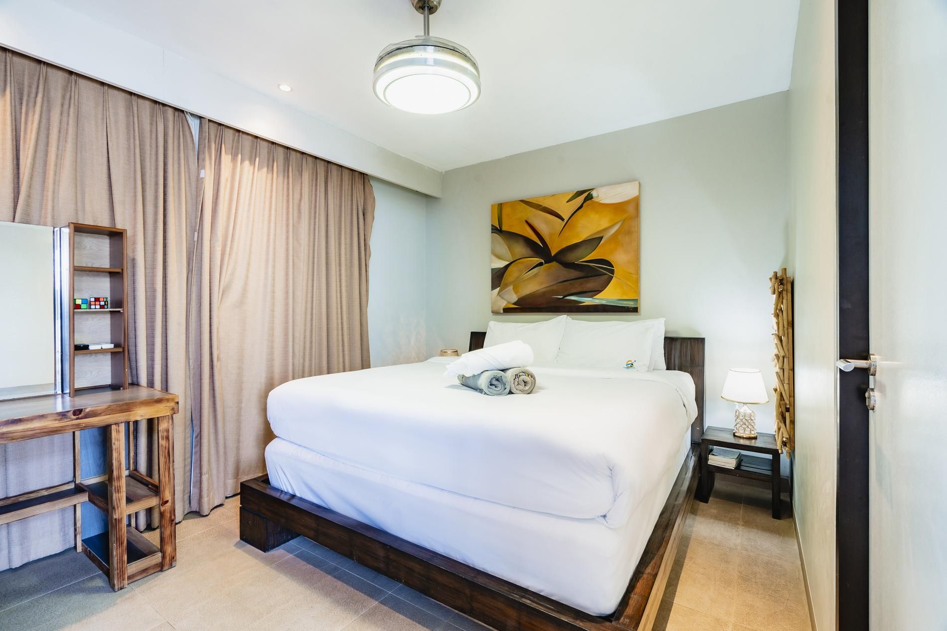 A hotel room with a bed, a desk, a lamp, and a painting on the wall.