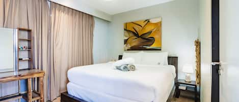A hotel room with a bed, a desk, a lamp, and a painting on the wall.