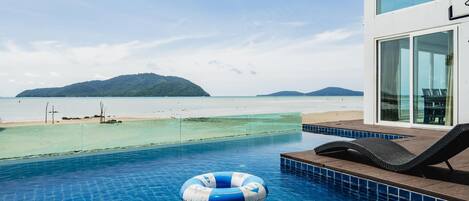 A swimming pool with clear water, a lounge chair, and a view of the beach and distant islands.