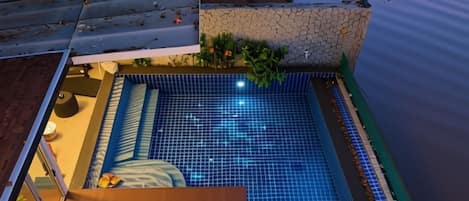 A swimming pool with a tiled edge, surrounded by a stone wall and a wooden deck.