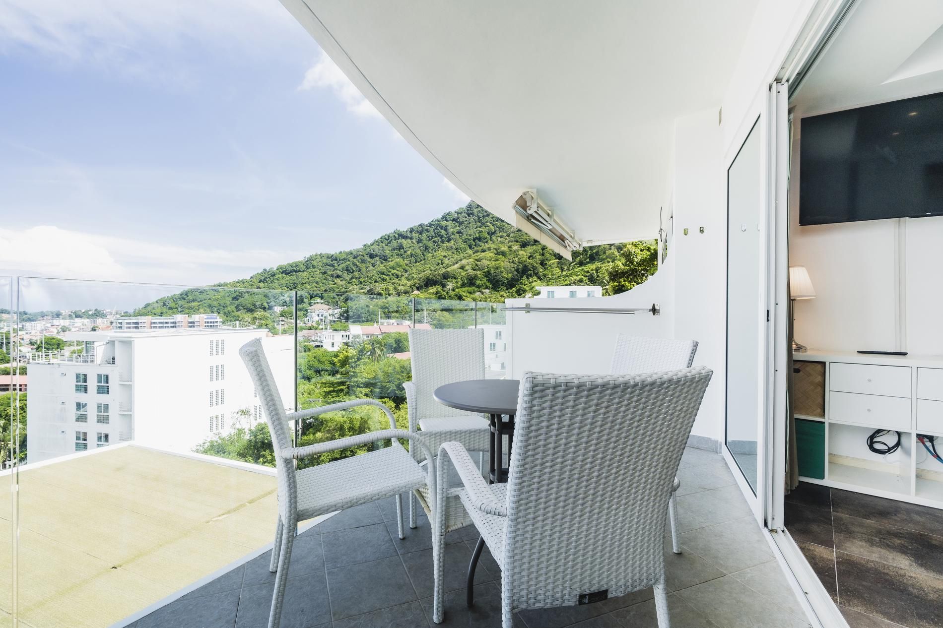 A balcony with a table and chairs, a TV, and a view of a hillside.