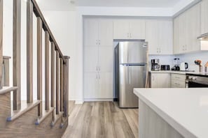Eine moderne Küche mit weißen Schränken, einem Edelstahlkühlschrank und einer Holztreppe.