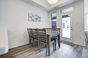 Un espace repas avec une table et des chaises en bois, un luminaire au plafond et une porte donnant sur l’extérieur.