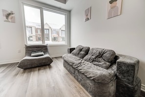 Un salon doté d’une grande fenêtre, d’un canapé gris, d’un fauteuil gris et de trois œuvres d’art accrochées au mur.