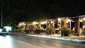 Ein Restaurant mit Außenbereich, Tischen und Stühlen, umgeben von Pflanzkübeln und beleuchtet mit Lichterketten.