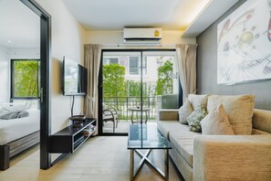 Een moderne woonkamer met een bank, een salontafel, een televisie en een balkon met uitzicht op groen.