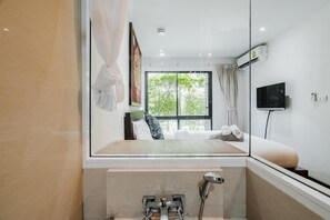 Een moderne badkamer met een douchecabine van glas, een wandgemonteerde televisie en een raam met uitzicht op groen.