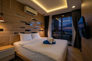 Una habitación de hotel moderna con una cama grande, un televisor de pantalla plana y vista a la ciudad al anochecer.