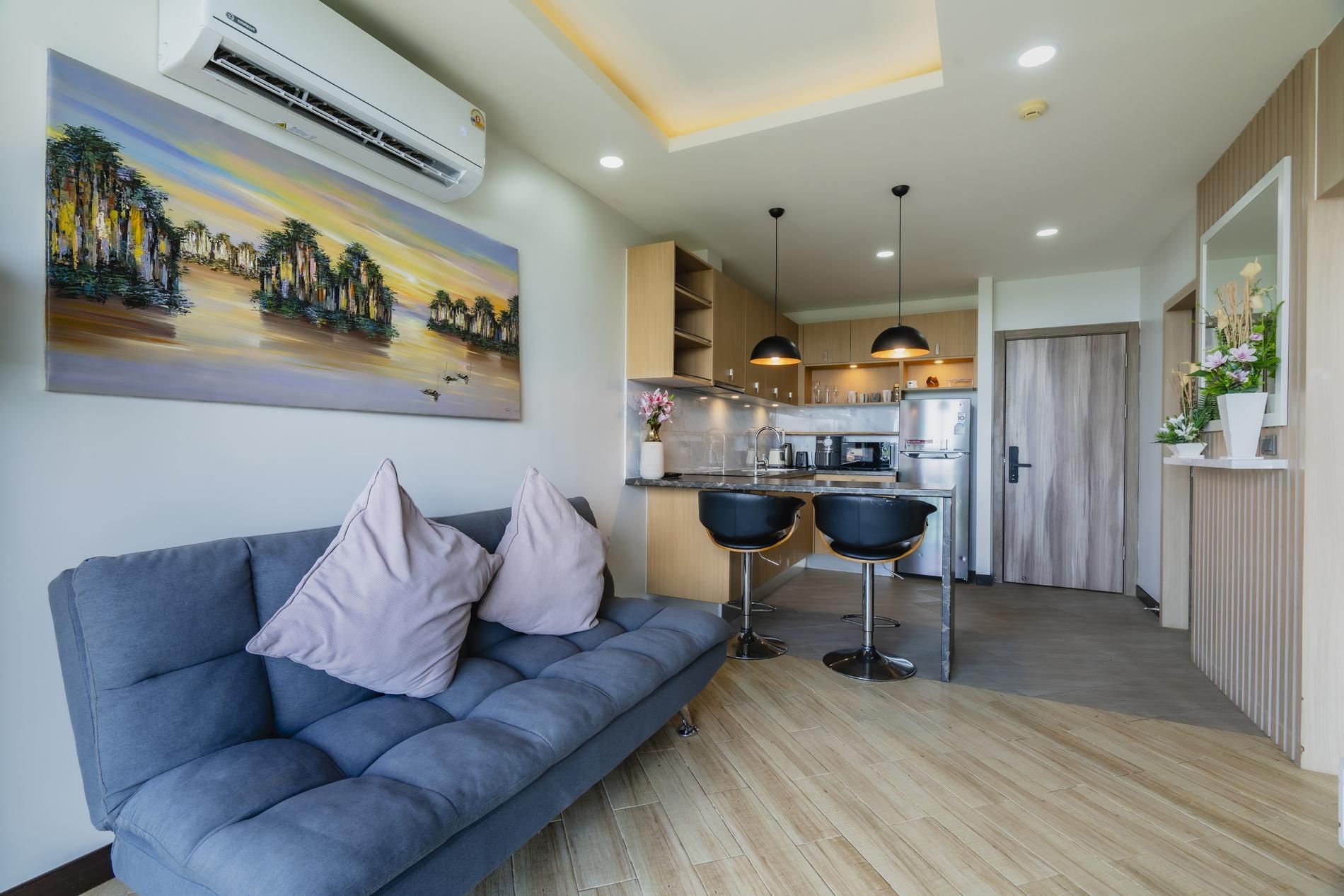 A modern living room with a sofa, two black bar stools, and a kitchen in the background.