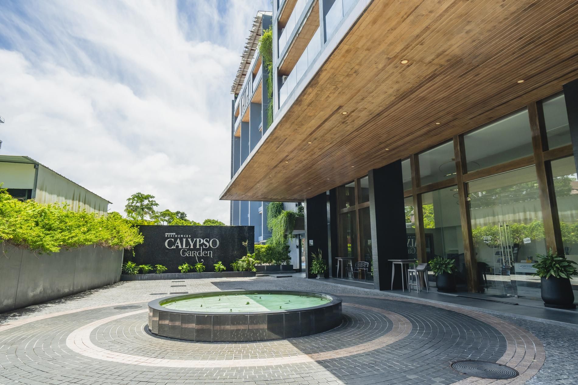 Un patio con una fuente, un letrero de Calypso Garden y la fachada de un edificio moderno.