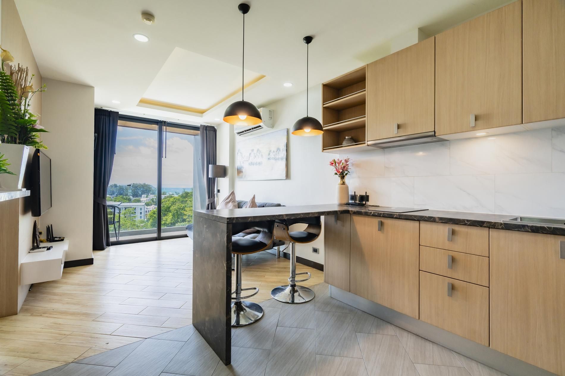 A modern kitchen with wooden cabinets, a marble countertop, and pendant lighting.
