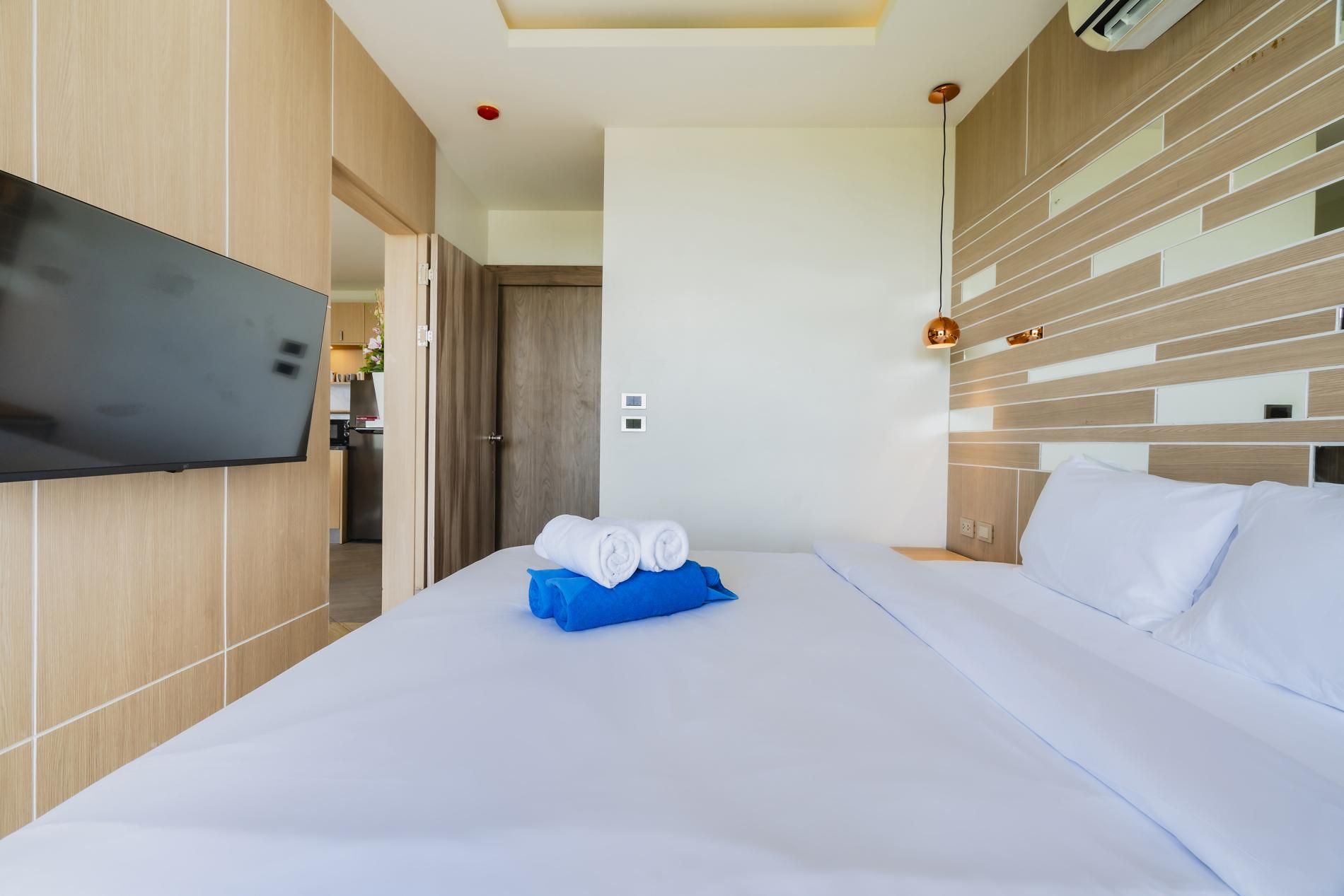 Una habitación de hotel con cama, televisor montado en la pared y cabecero de madera.