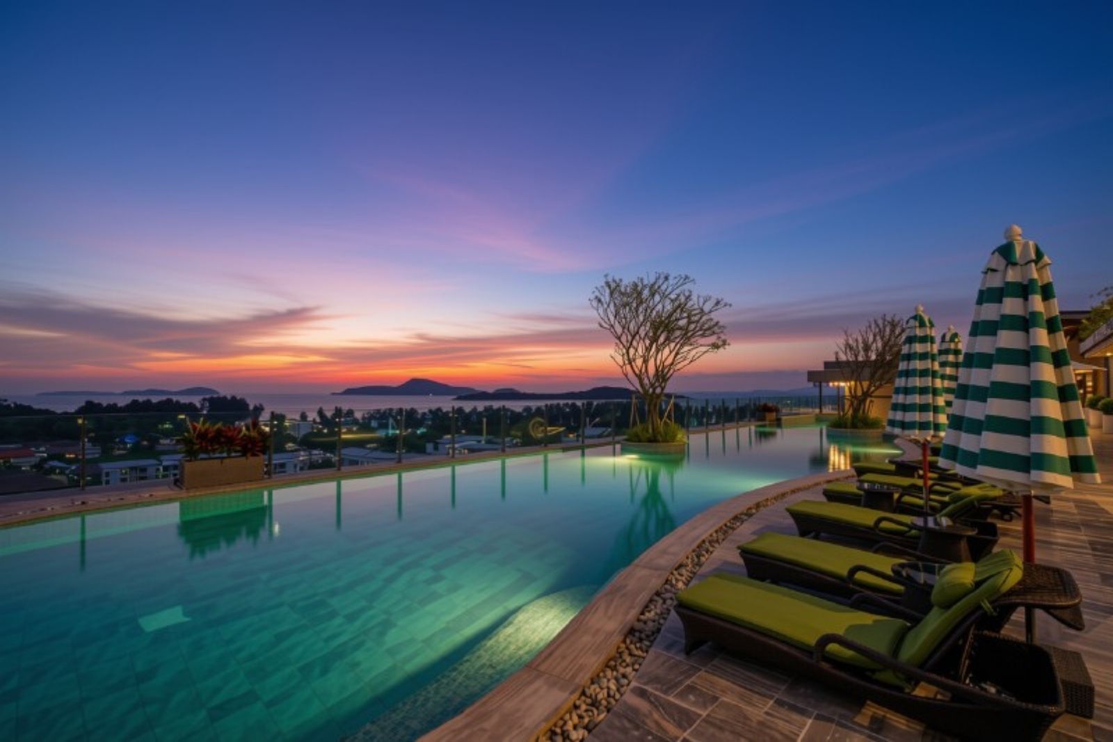 Une piscine entourée de chaises longues et de parasols, elle-même bordée d’un espace paysager offrant une vue sur le coucher du soleil et les montagnes lointaines.