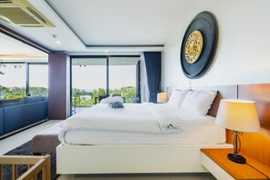 A hotel room with a large bed, a bedside table with a lamp, a view of greenery outside, and a modern ceiling design. - At The Tree Sea View 1BR Walk To Rawai Beach (Rawai)