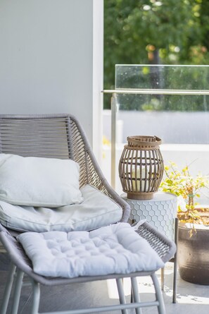 A balcony with a wicker chair, a small table with a candle, and a potted plant. - At The Tree Sea View 1BR Walk To Rawai Beach (Rawai)