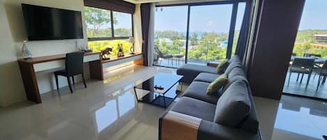 A modern living room with a flat-screen TV, a sofa, a coffee table, and a balcony with a view.