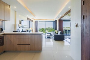 Eine moderne Küche mit einer zentralen Kochinsel, ein Essbereich mit einer Couch und Blick auf Grün durch große Fenster.