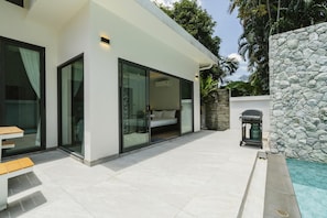 Een modern huis met een glazen deur die leidt naar een slaapkamer, een stenen muur en een zwembadgedeelte.