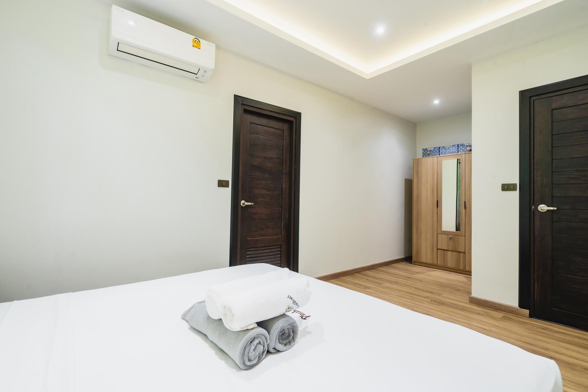 A hotel room with a bed, a wooden floor, a wardrobe, and an air conditioning unit.