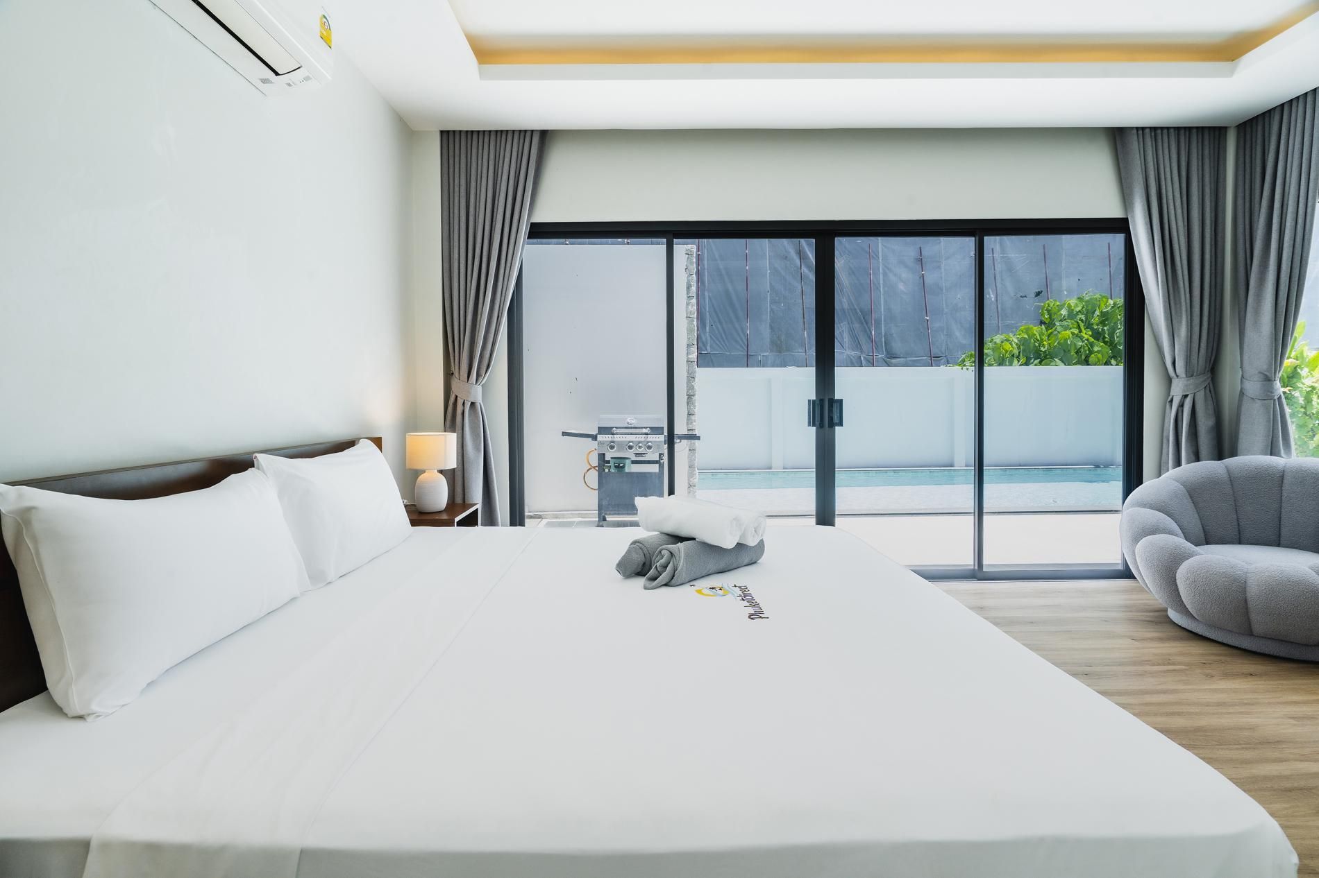 A hotel room with a large bed, a bedside table with a lamp, a view of a swimming pool, and a chair.