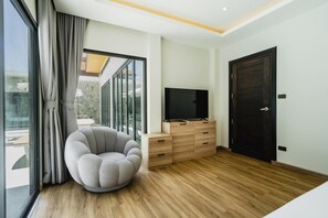 Een moderne woonkamer met een ronde grijze fauteuil, een houten tv-meubel en een donkerhouten deur.
