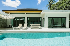 Een modern huis met een zwembad, een terras met lounge stoelen en een grote schuifpui.