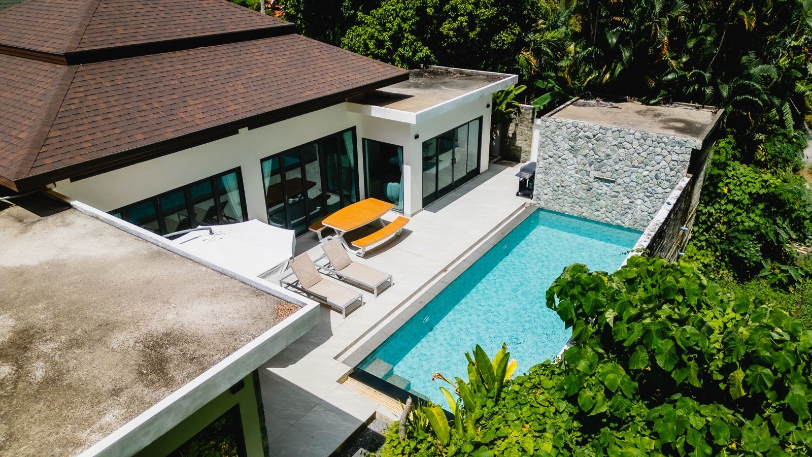Et moderne hus med swimmingpool, store vinduer og udendørs siddepladser.