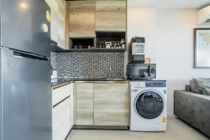 A compact kitchen with a built-in washing machine, a coffee machine, and a refrigerator. - Best Seaview 1 Bed Condo Sky Garden Rawai Beach (Rawai)