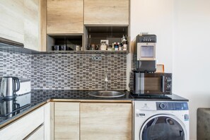 Une cuisine compacte équipée d’un évier, d’une machine à café, d’un four à micro-ondes et d’un lave-linge.