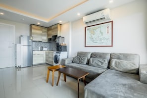 A modern living room with a grey sofa, a wooden coffee table, and a kitchen area with a refrigerator, microwave, and washing machine. - Best Seaview 1 Bed Condo Sky Garden Rawai Beach (Rawai)