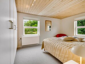 Een slaapkamer met een bed, een rood kussen, een spiegel en een raam met uitzicht op groen.