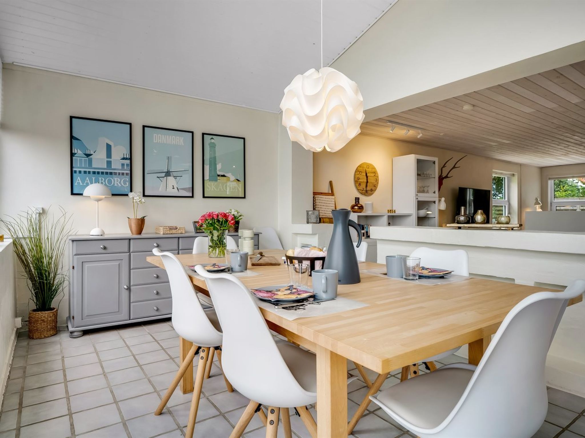 Ett modernt kök med en matplats, med ett träbord, vita stolar och en hängande lampa.