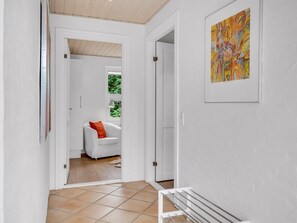 Een gang met een witte deur die leidt naar een kamer met een witte bank en een rood kussen.