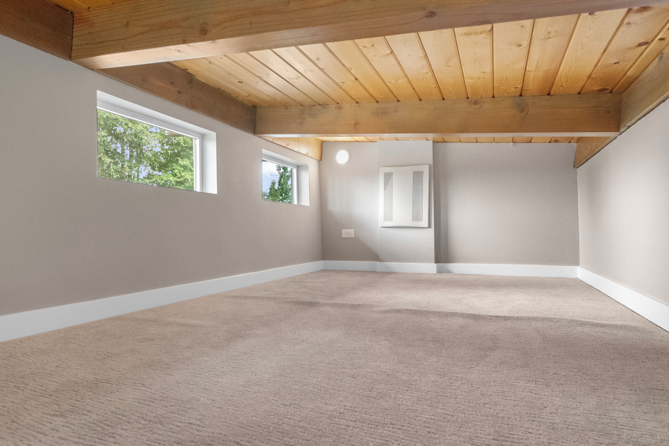 Una habitación con techo inclinado, dos ventanas y suelo alfombrado.