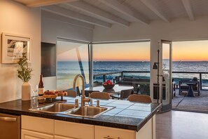 A modern kitchen with a large window overlooking the sea, a dining area with a view, and a bar area.