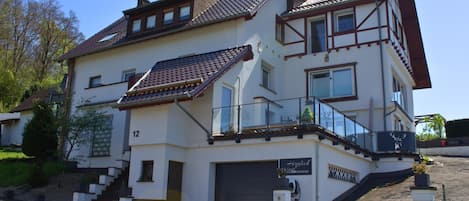 A two-story building with a tiled roof, a garage, and a sign that reads 'Herzlich Willkommen'.