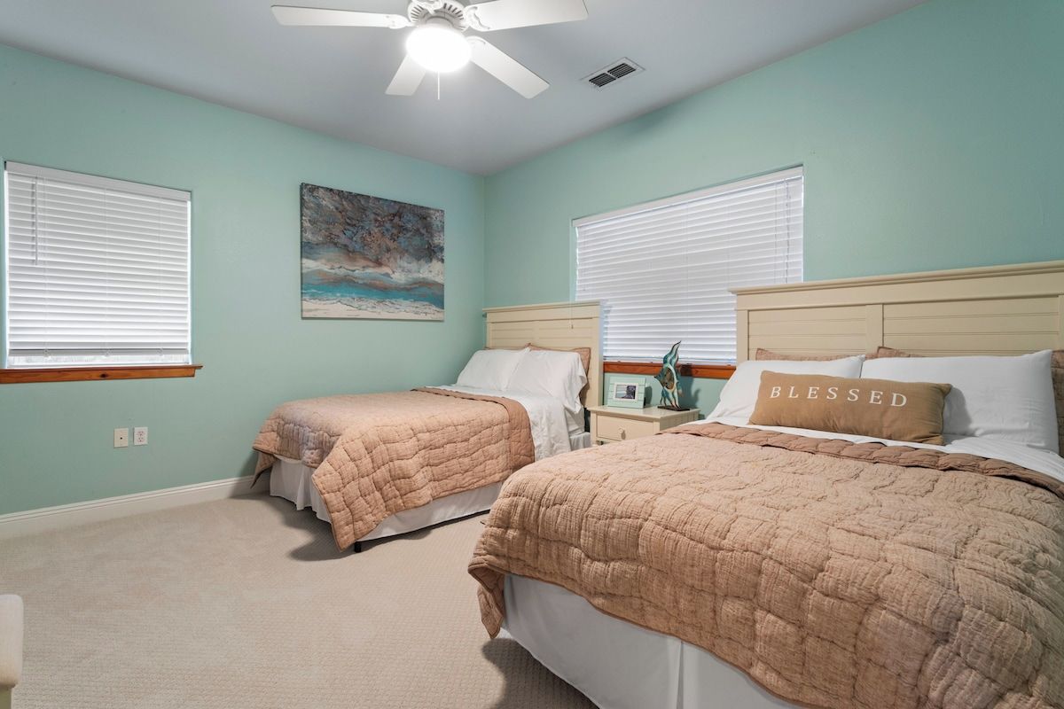 A bedroom with two beds, a ceiling fan, and a painting on the wall.